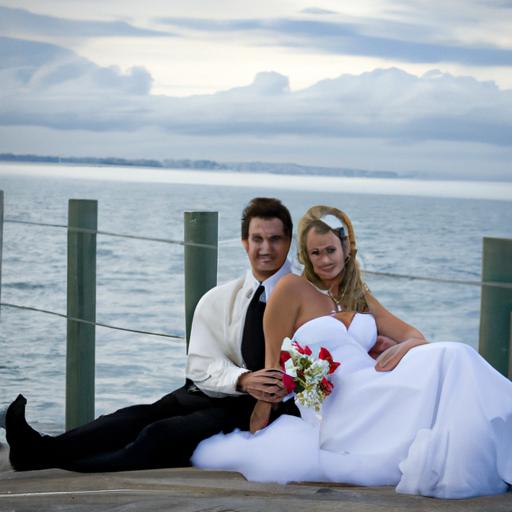 Cặp đôi ngồi trên bến tàu, phía sau là khung cảnh biển xanh biếc và trời xanh ngắt, tạo nên bức ảnh cưới đầy lãng mạn và sâu lắng.